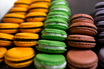 Macaroons on a black background, a lot of colorful pasta with French cookies. Beige, brown French macarons on a stand.