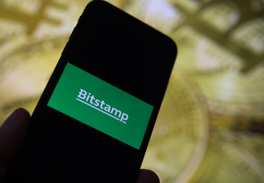 Viersen, Germany - February 9. 2021: Closeup of mobile phone screen with logo lettering of bitstamp trading platform, blurred bitcoins background
