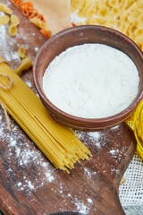 Variety of dry pasta with oil and flour on a gray background
