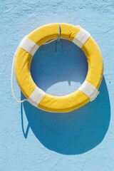 Yellow circular lifebuoy hanging on blue wall in a sunny day