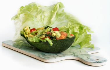 avocado tomato salad with cucumber and green iceberg lettuce served in avocado on the background of green iceberg lettuce