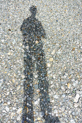 Long shadow of man standing on stony riverbed.