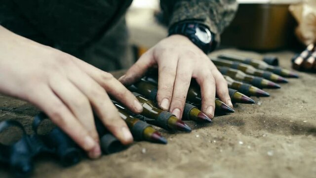 Inserts large-caliber bullets into the machine-gun belt. Close up. A lot of bullets and ammunition.