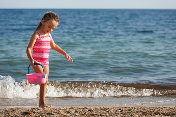 bambina bionda con gli occhi verdi gioca con la sabbia al mare in costume da bagno