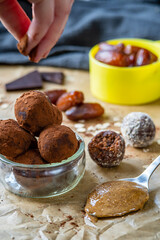 Hand sprinkles cocoa powder on healthy energy protein balls with dates, oats, peanut butter and dark chocolate. Homemade gluten free truffle bites with no bake. Vegan raw appetizer or snack. Side view