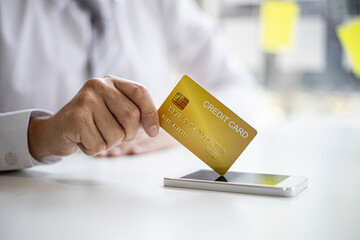 A businessman with a yellow credit card, uses his credit card to pay for goods and services through a smartphone app, nowadays card payments are widely used around the world. Credit card concept.