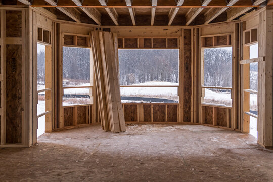 Interior view of a semi circular sun room  letting in a lot of light, plywood floors and room skeleton structure at a new American real estate development construction site
