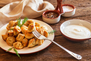 Dumplings with meat, onion and sour cream, on a plate with Chinese chopsticks, on wooden background.