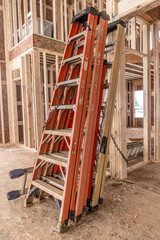 Fototapeta premium Red, orange, yellow tall aluminum construction ladders leaning on each other in the living room of a luxury house under construction in the USA 