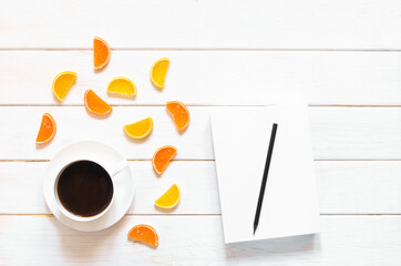 white cup of coffee, white paper and multicolored fruit marmalade lie on a white wooden background