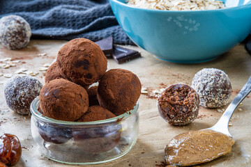 Healthy energy protein balls with dates, oats, peanut butter and dark chocolate. Homemade gluten free truffle bites covered with cocoa powder or almonds. Vegan raw appetizer or food snack. Side view.