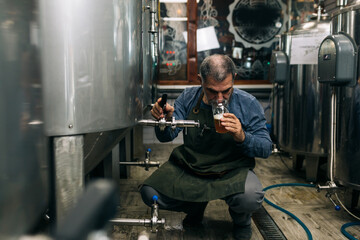 Obraz na płótnie Canvas brewer examining taste and color of the beer in his craft beer brewery