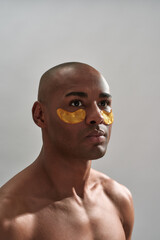 Muscular naked man looking after bags under eyes with patches