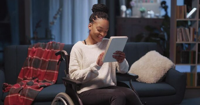 Joyful african american young woman disabled girl sitting in qheelchair using cellphone online apps communicating with friends online staying home.