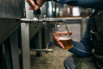 brewer working in his craft beer brewery. he is pouring the beer in a glass