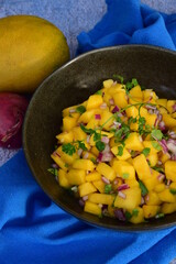 Fresh homemade mango salsa in a bowl on blue background