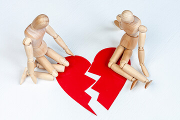two wooden mannequins sitting near a red broken heart