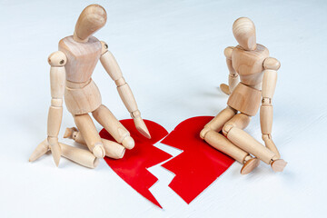 two wooden mannequins sitting near a red broken heart