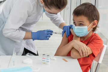 boy in medical mask with his eyes turned up is waiting for doctor to finish injection of vaccine....