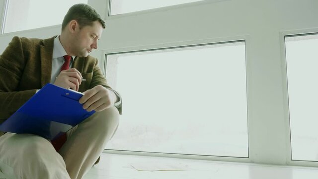 A man sitting by the window makes notes with a pen. A businessman looks at financial charts. Empty space.