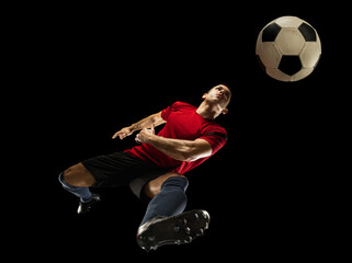 Naklejka premium Young caucasian football, soccer player in action, motion isolated on black background, look from the bottom. Concept of sport, movement, energy and dynamic, healthy lifestyle. Training, practicing.