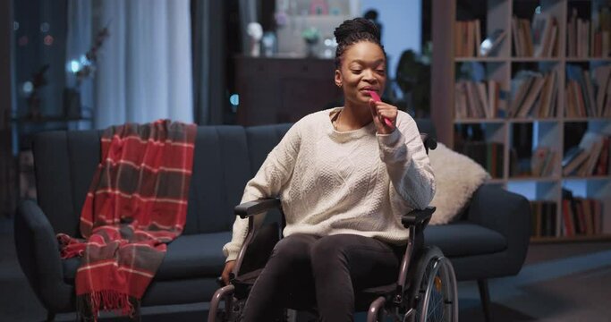 Joyful african american woman sitting in wheelchair singing happy song ejoying music swinging around room. Home entertainment. leisure concept.