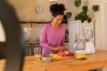 Happy caucasian woman vlogging, cutting fruit in kitchen at home