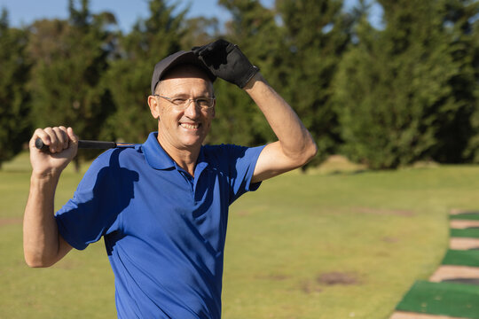 Portrait of caucasian senior man holding golf club looking at camera and smiling