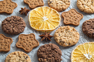 Oatmeal, ginger and chocolate cookies, slices of dried oranges, stars of anise lie on a textured gray background. Fragrant and delicious sweet pastries