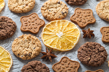 Oatmeal, ginger and chocolate cookies, slices of dried oranges, stars of anise on a textured gray background. Side view
