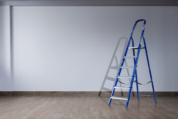 A dirty blue metal stepladder against of drywall gray painted  in a new building. The concept of professional renovation. Copy space.