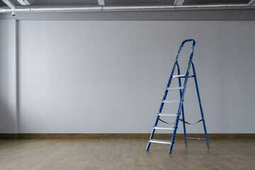 A dirty blue metal stepladder against of drywall gray painted  in a new building. The concept of professional renovation. Copy space.