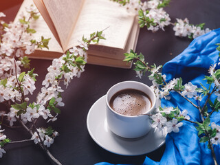 Obraz na płótnie Canvas Springtime, a white cup of espresso coffee on a dark stone table, white cherry blossoms, and a book. Read a book on a weekend morning