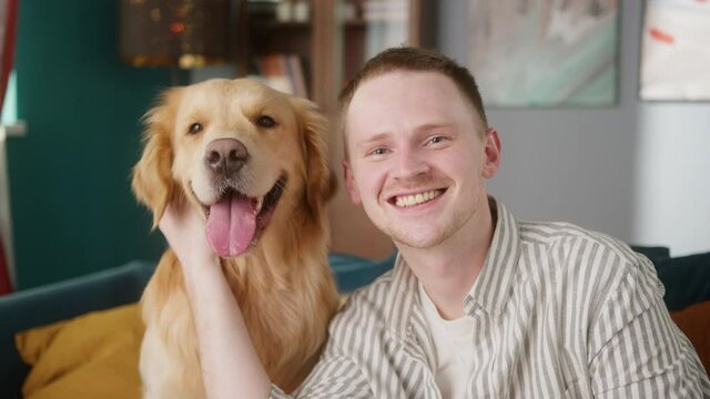 British redhead man together with dog retriever making selfie photo or video call on front camera smartphone. Positive young student man conference call with pet for blog.