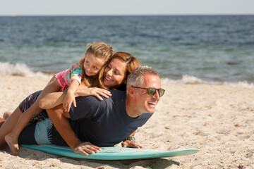 Fototapeta premium Allegra famiglia composta da padre, madre e figlia si diverte giocando con con una tavola da surf in spiaggia al mare