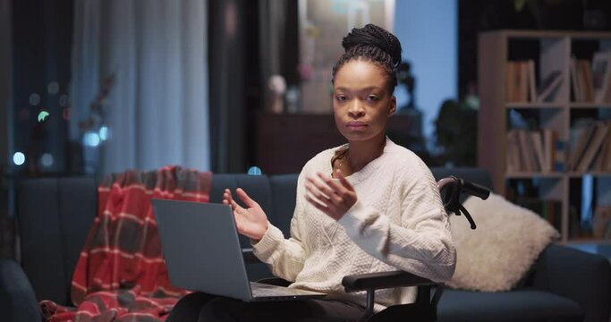 Portrait of pretty african black girl with disabilities holding laptop on wheelchair staying at home. Disabledw female. Job opportunities. Freelancer lifestyle.