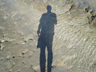 Man and shadow on rocky beach.