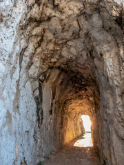 Obraz premium chemin de randonnée passant dans un tunnel creusé dans la roche et avec le soleil inondant la sortie