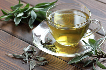 Sage herbal tea in a glass cup with fresh and dried leaves on rustic wooden background, closeup,...