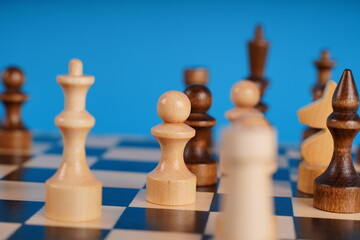 White and black wooden pieces on a chessboard. A chessboard set up during a game on a blue background.