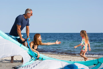 Famiglia composta da padre, madre e una figlia si prepara il kitesurf in spiaggia pronti per...