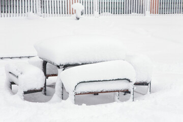 Snow drifts lie on the table and benches in the snow-covered courtyard of the city. Winter city landscape.