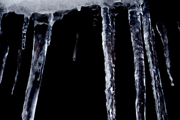 Naklejka na ściany i meble Sharp and dangerous icicles isolated on black background. Cold weather. Winter concept.