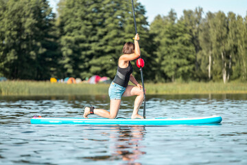 Young woman doing yoga or fitness on sup or stand up paddle board in summer day. concept of harmony with the nature, free and healthy living, freelance, remote business.