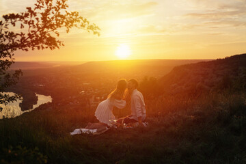 Silhouette of loving couple kissing at sunset, having a romantic picnic on the hill. 