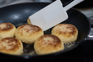 cheesecakes are fried in a frying pan the cook turns the dough with a spoon close up the background is blurred