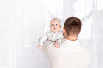 a father holds a newborn baby on his shoulder at home by the window, the concept of a happy loving family, father's day