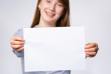 Woman with a piece of blank, empty space, paper sheet in her hand for your ad. Surprised woman shows a poster, canvas, white sheet of paper isolated on gray background