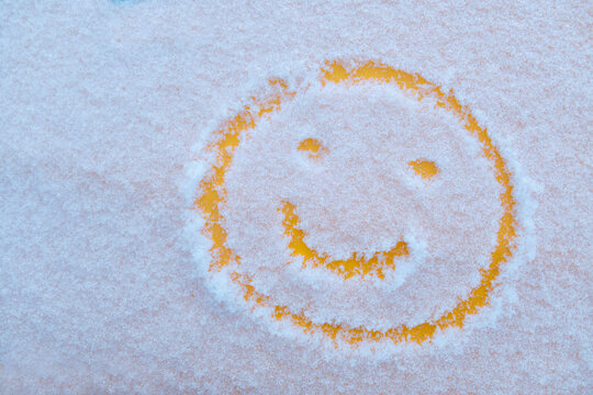 Snow background. Wet snow texture with a pattern of a cheerful emoticon in a winter and yellow background, outdoors close-up. Smile in the snow, cheerful cheerful image. Winter time concept.