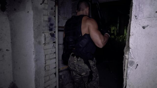 The gunman walks through an abandoned building and approaches a broken window holding a submachine gun cocked